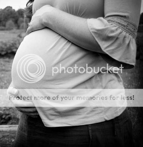 Image shows a woman holding her pregnant belly outdoors