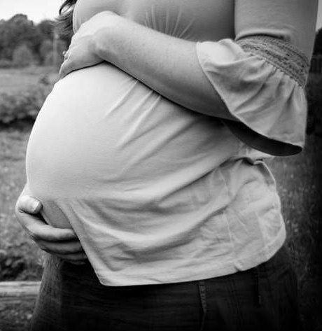 Photo shows a pregnant woman embracing her belly outdoors